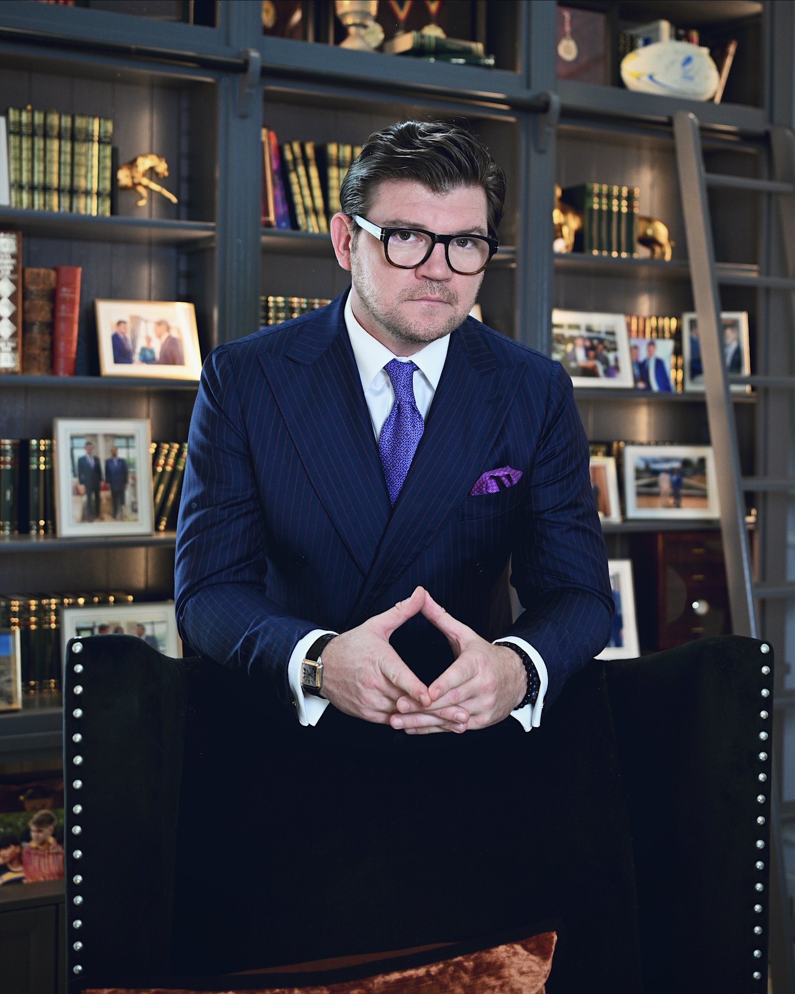 Anton Pisaroglu seated in a navy suit before bookshelves, with his hands together.