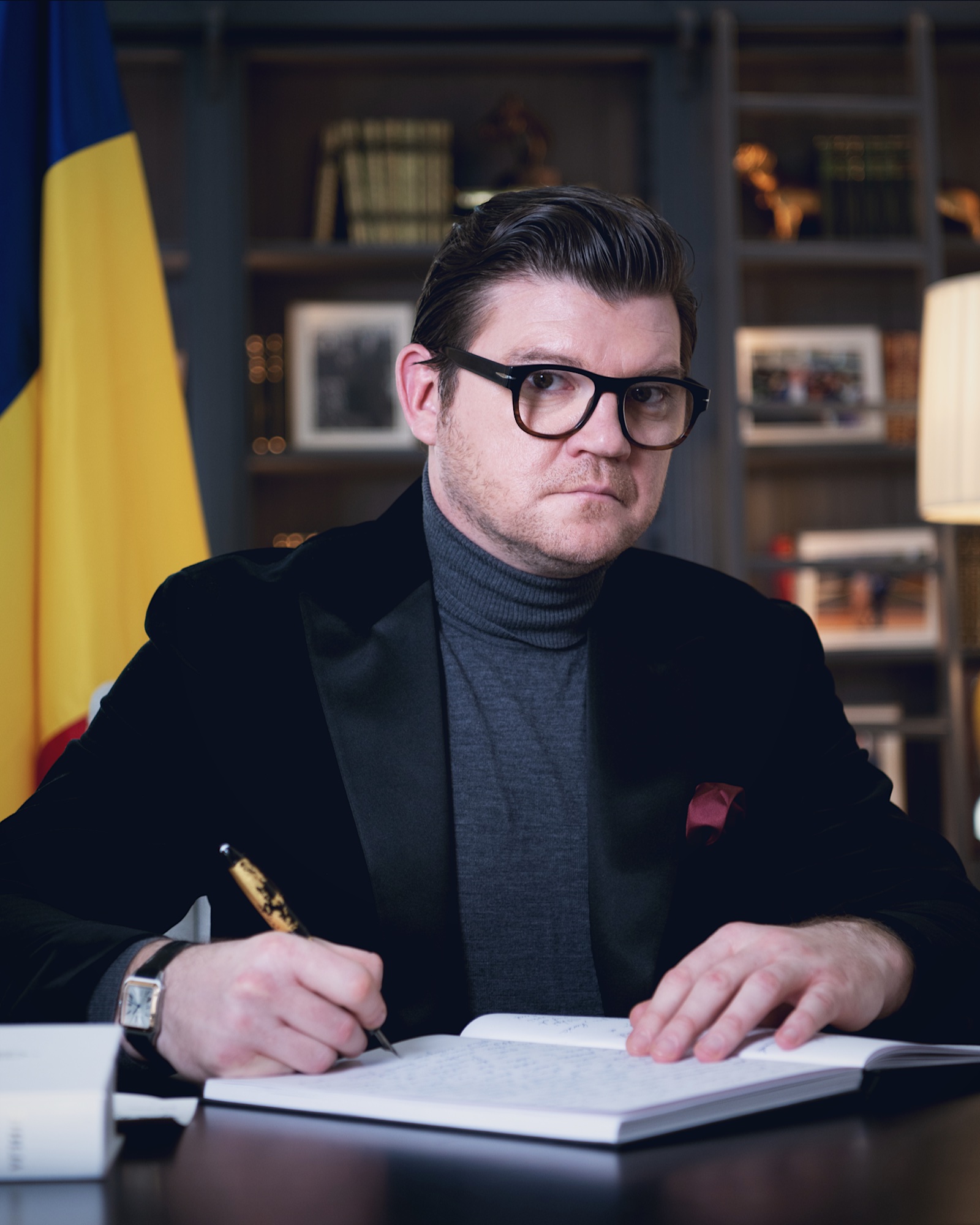 Anton Pisaroglu writing in a notebook at a desk, with a Romanian flag beside him.
