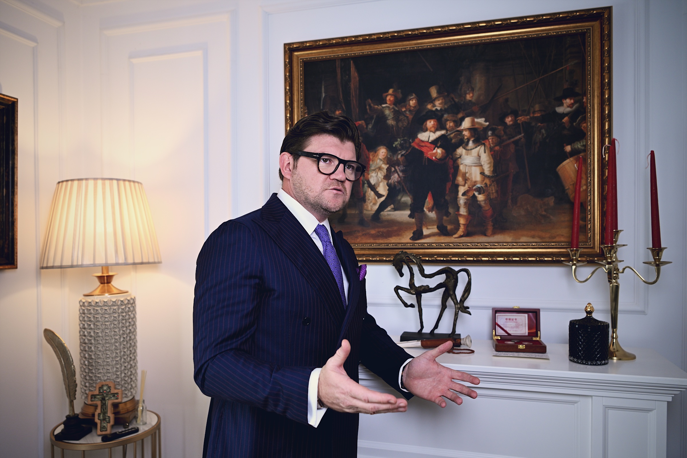 Anton Pisaroglu gesturing beside a large framed painting.