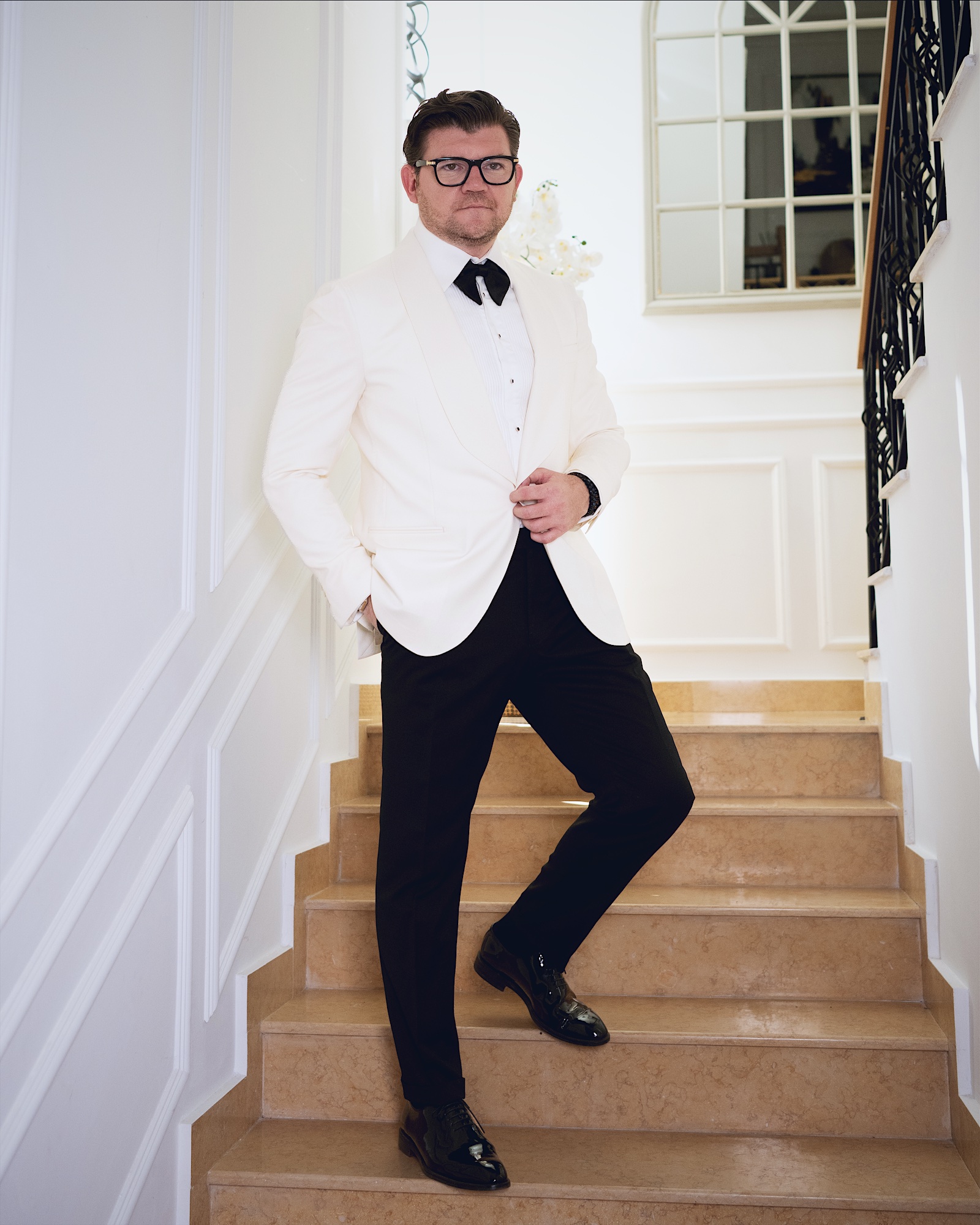 Anton Pisaroglu in a white dinner jacket and black bow tie, standing on a staircase.