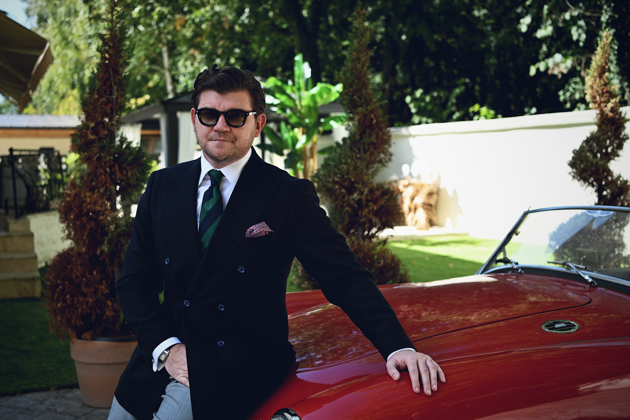 Anton Pisaroglu standing beside a red convertible in an outdoor courtyard.
