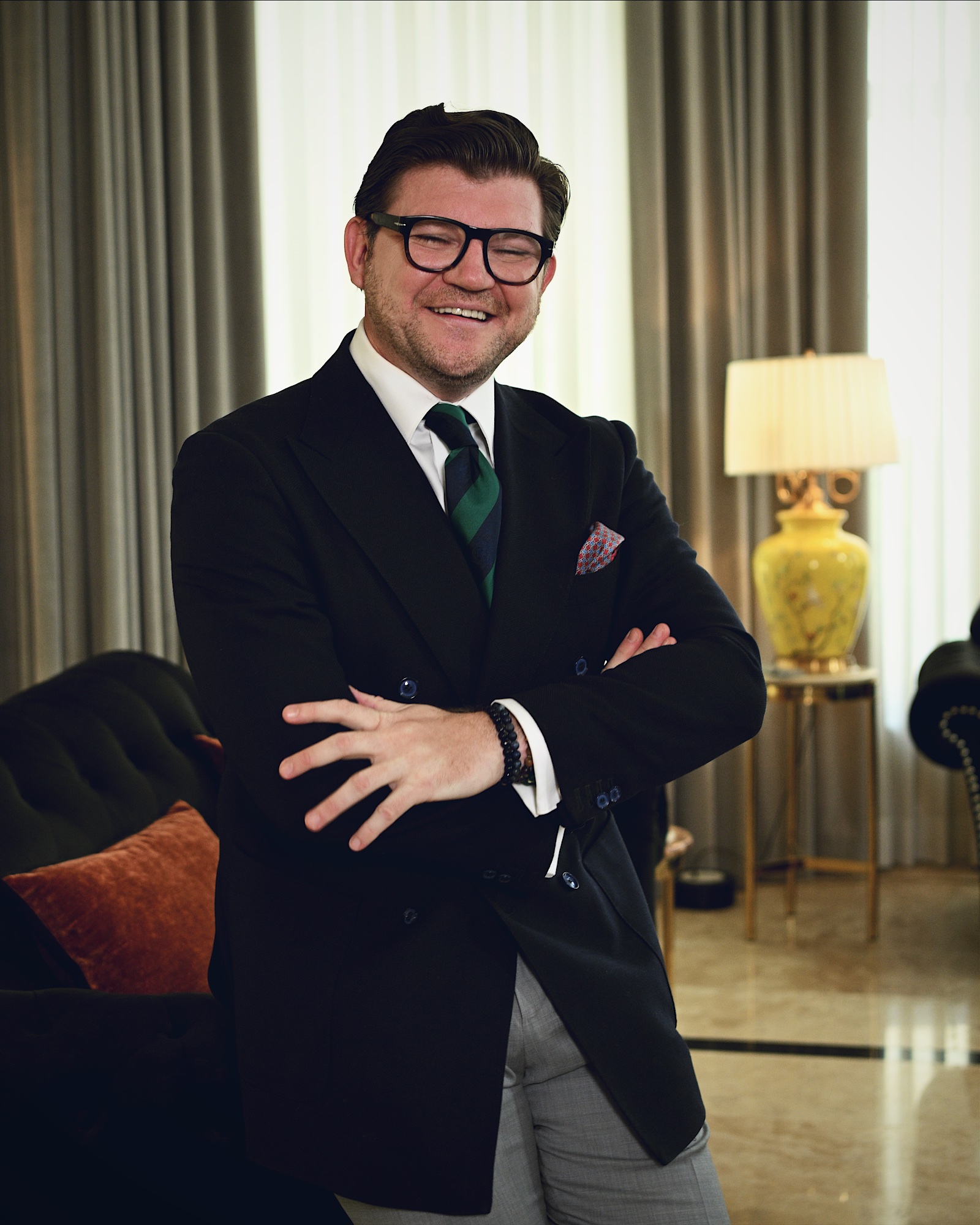 Anton Pisaroglu smiling with his arms folded, wearing glasses and a dark blazer in a sitting room.